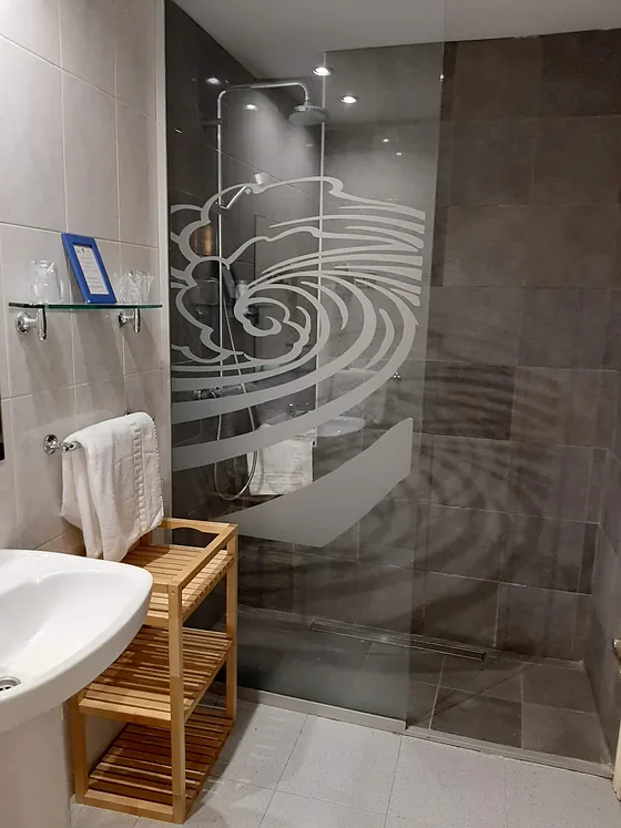 Baño con ducha y una ola grabada a tamaño grande en la mampara de cristal.