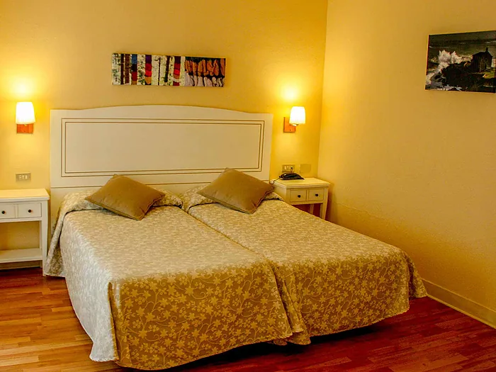 Habitación de paredes amarillas con dos camas juntas, dos apliques encendidos y teléfono en la mesilla.