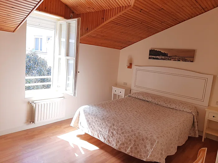 Habitación abuhardillada del hotel, con el techo de madera en pendiente y la ventana abierta a la calle.