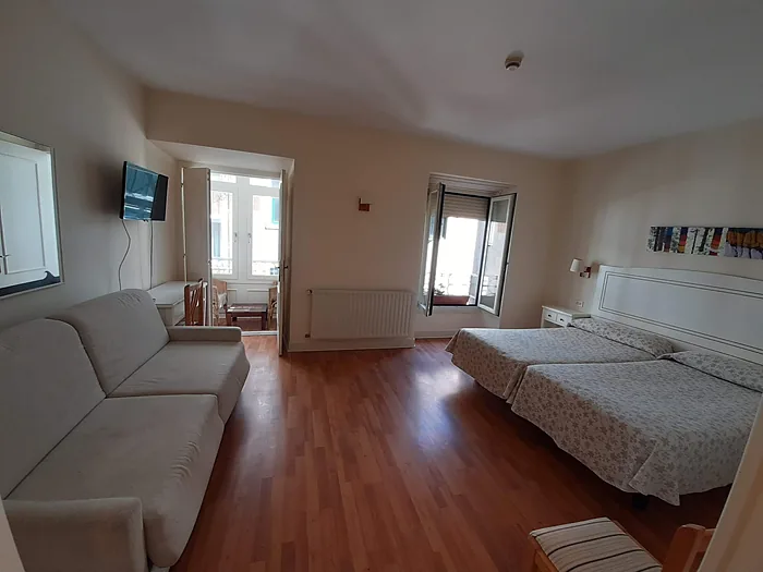 Habitación amplia con sofá, televisión en la pared y una segunda estancia al fondo.