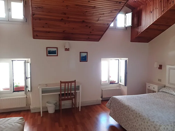 Habitación con mesa y silla junto a la ventana, y el techo de madera en pendiente.